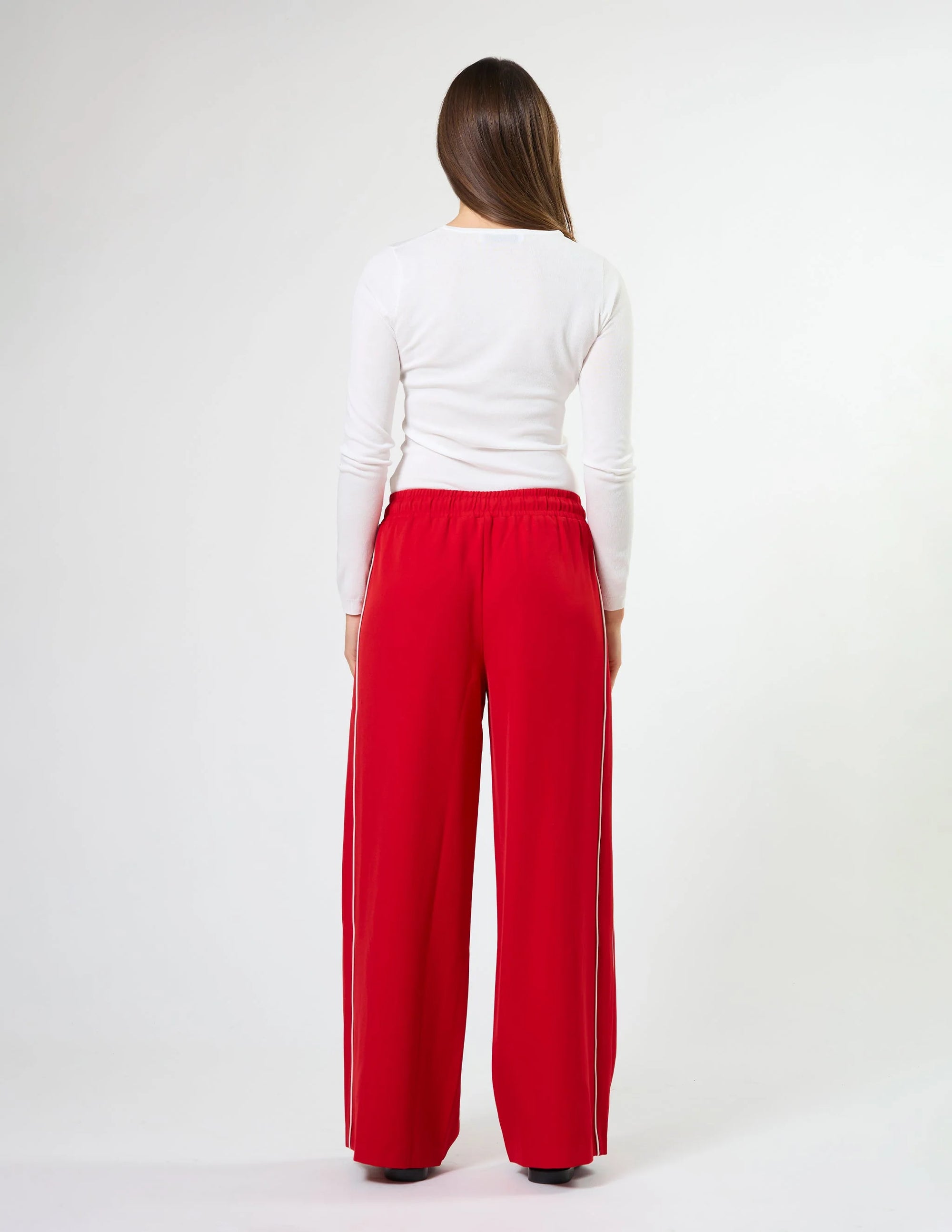 Woman wearing wide leg red pants with drawstrings and white stripes on sides by brand Stella & Gemma on a white background back view