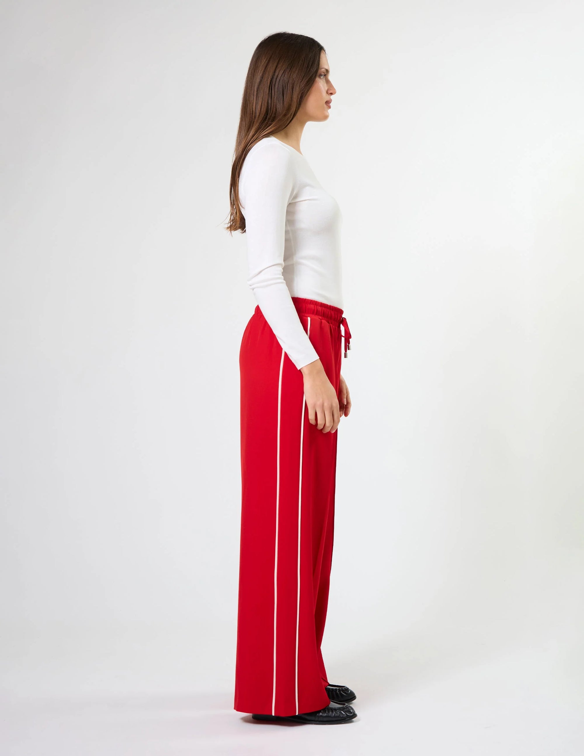 Woman wearing wide leg red pants with drawstrings and white stripes on sides by brand Stella & Gemma on a white background side view 